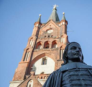 <p>Paul Gerhardt Statue vor dem Kirchturm der St.-Moritz-Kirche Mittenwalde PGW Etappe 5</p>