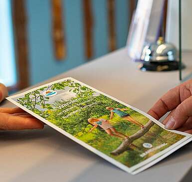 <p>Mitarbeiter der Touristinfo übergibt Infobroschüre an Kunde</p>